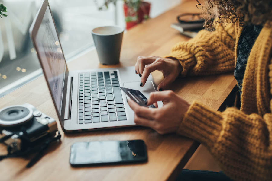 Woman sitting at a table, using a laptop while holding a credit card, focused on online shopping.